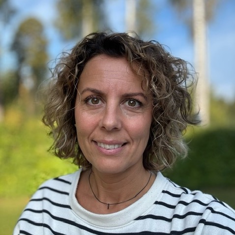 En kvinna sitter utomhus, tittar in i kameran och ler